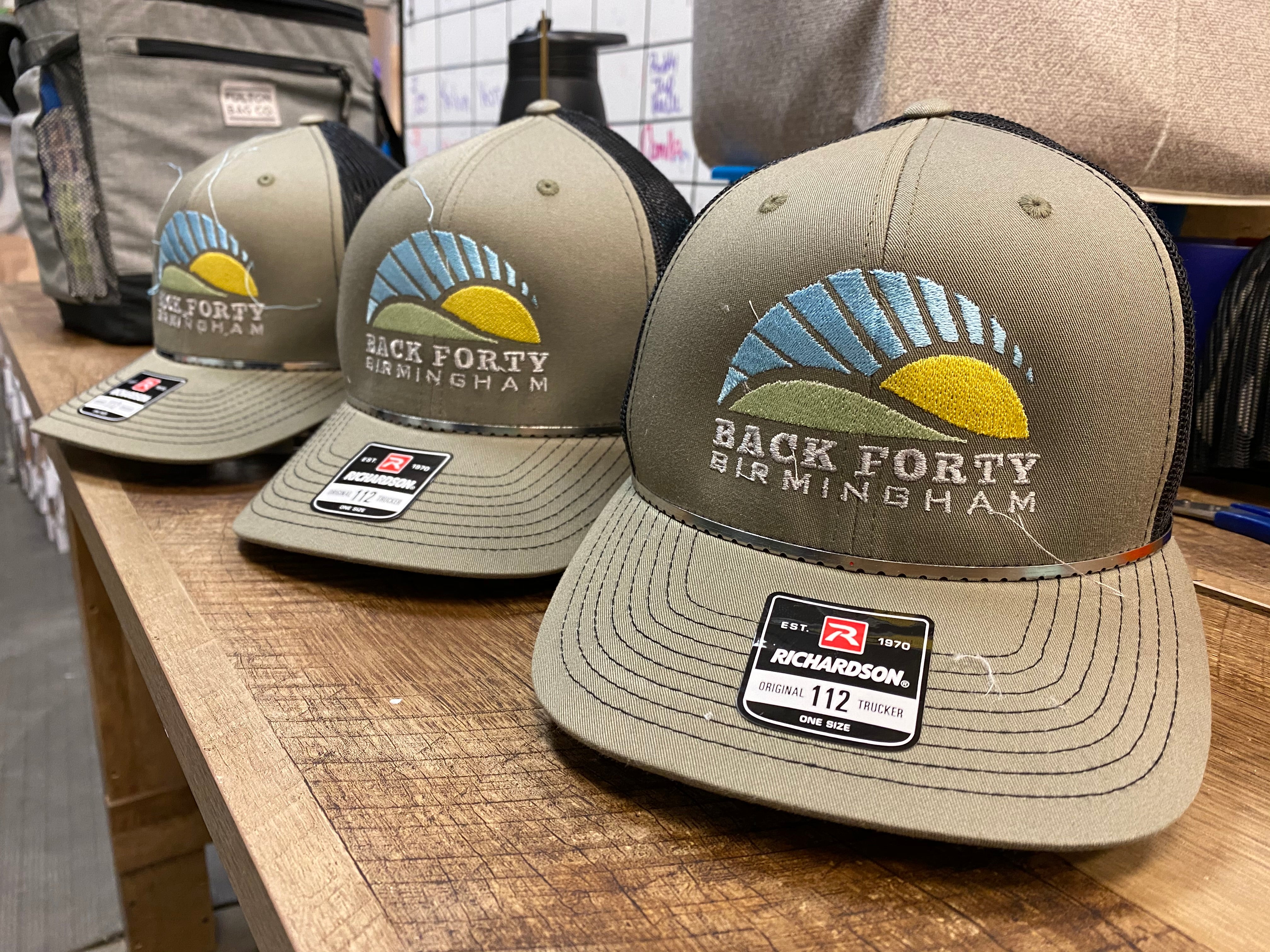 Back Forty Beer Co Birmingham embroidered trucker caps with sunrise mountain logo on olive green, stitched at Presto Embroidery Birmingham