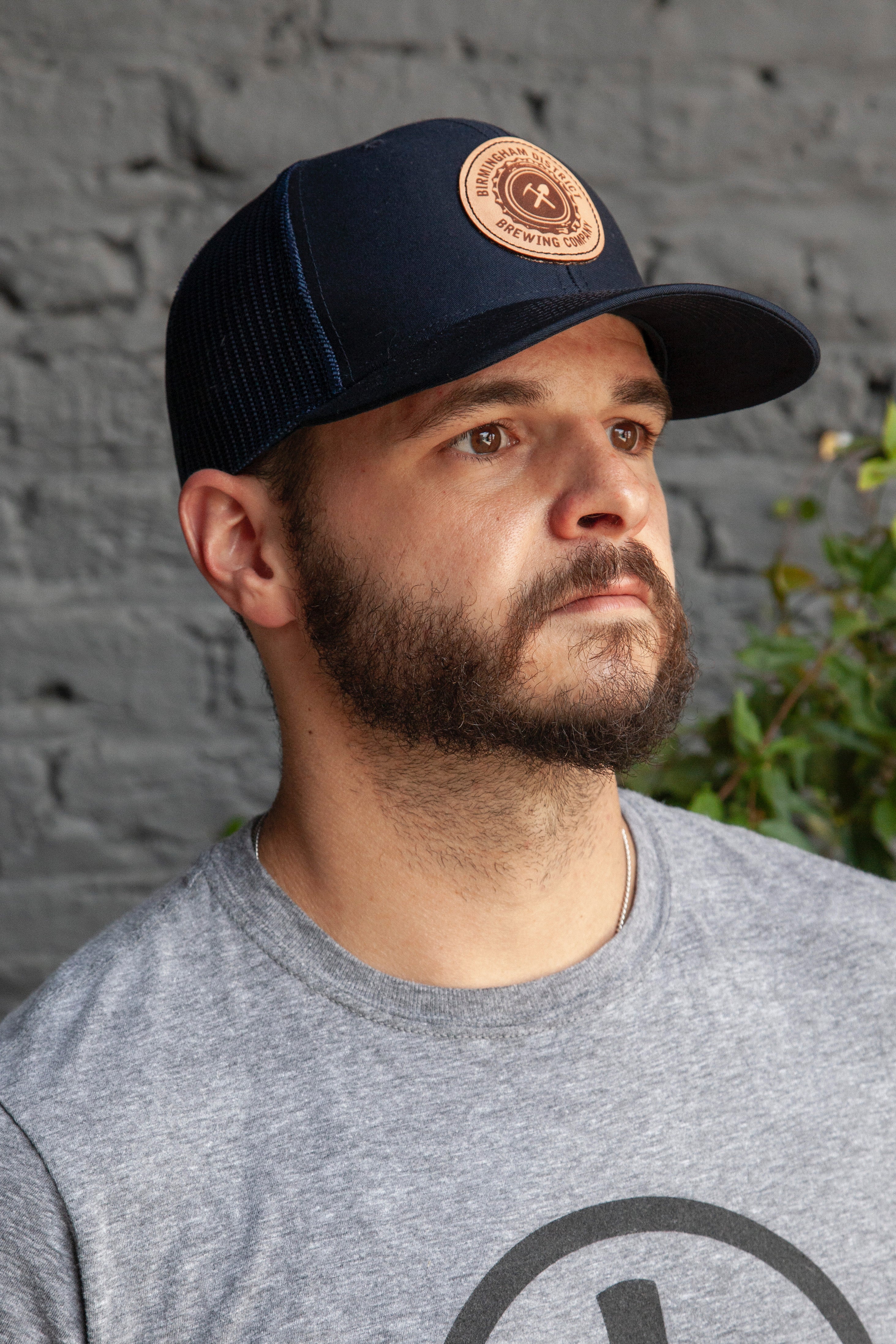 Customer wearing Birmingham District Brewing navy embroidered leather patch trucker cap and grey tee with brewing company logo, embroidery by Presto Embroidery