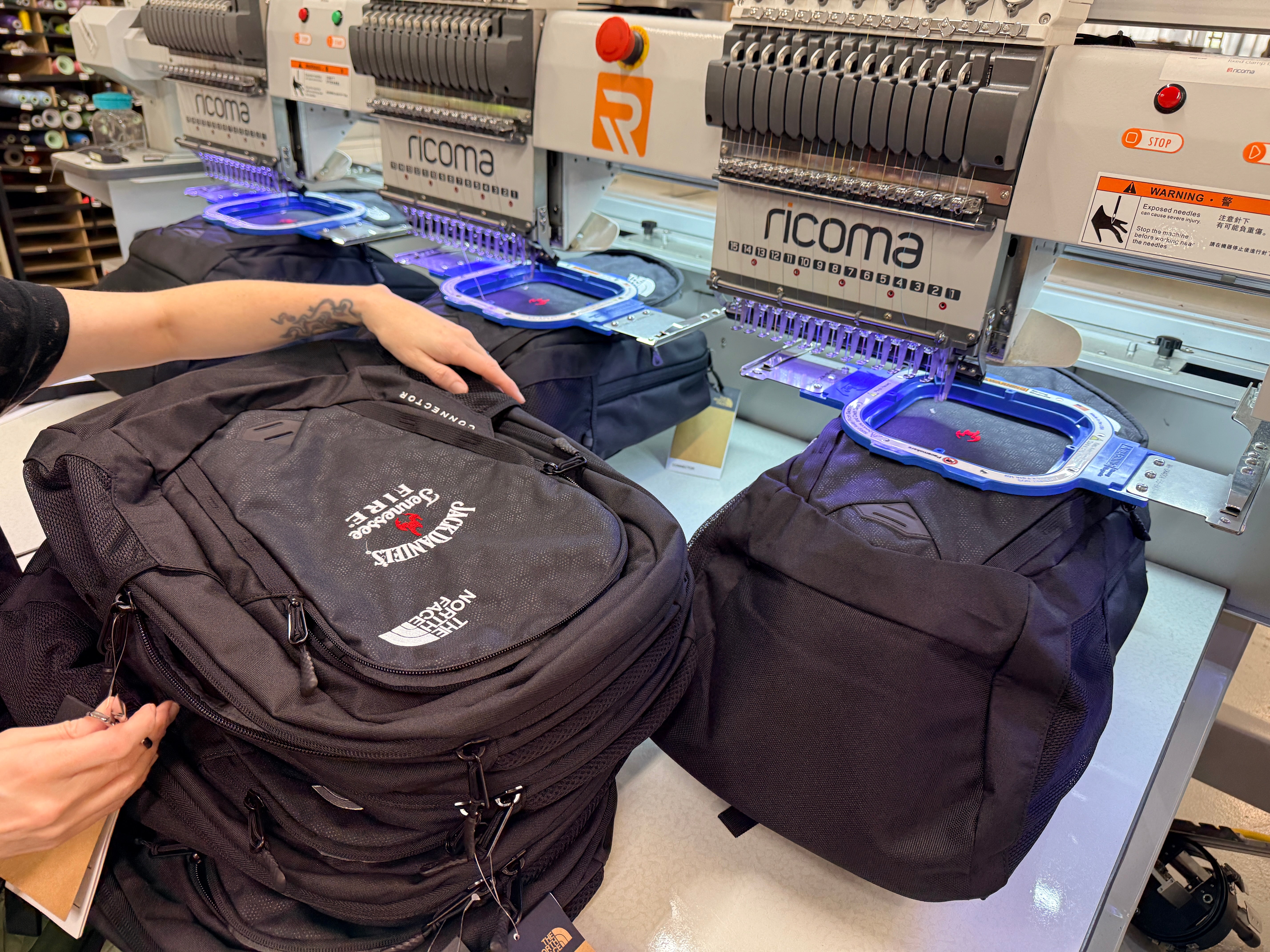 Ricoma multi-head commercial embroidery machine running custom embroidered black backpacks at Presto Embroidery Birmingham AL